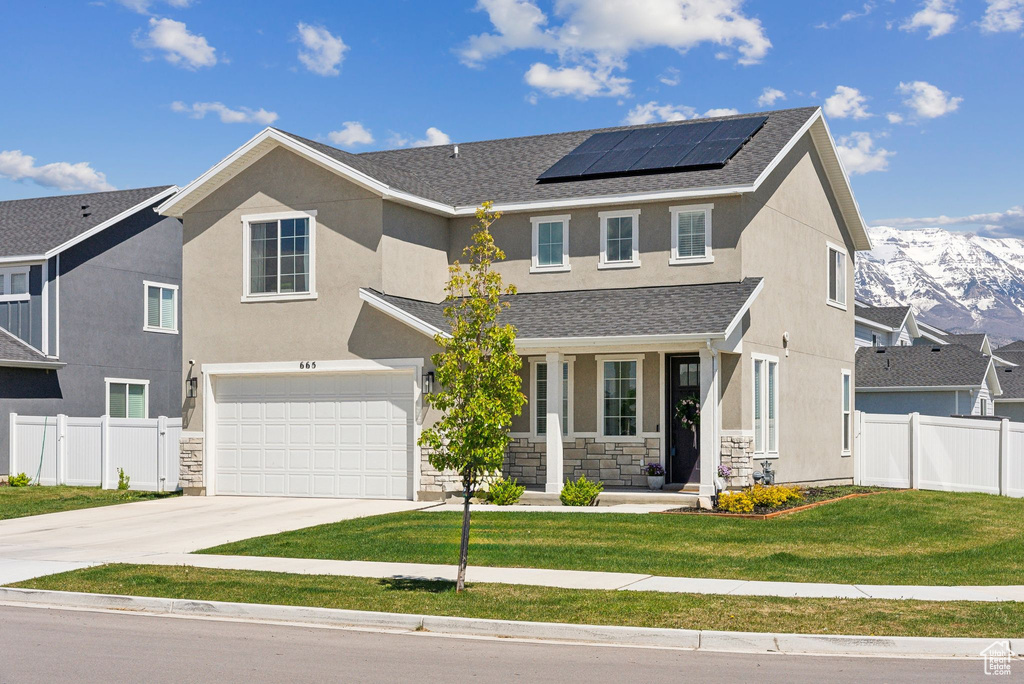 View of front facade featuring fence, roof mounted solar panels, a porch, and a front yard