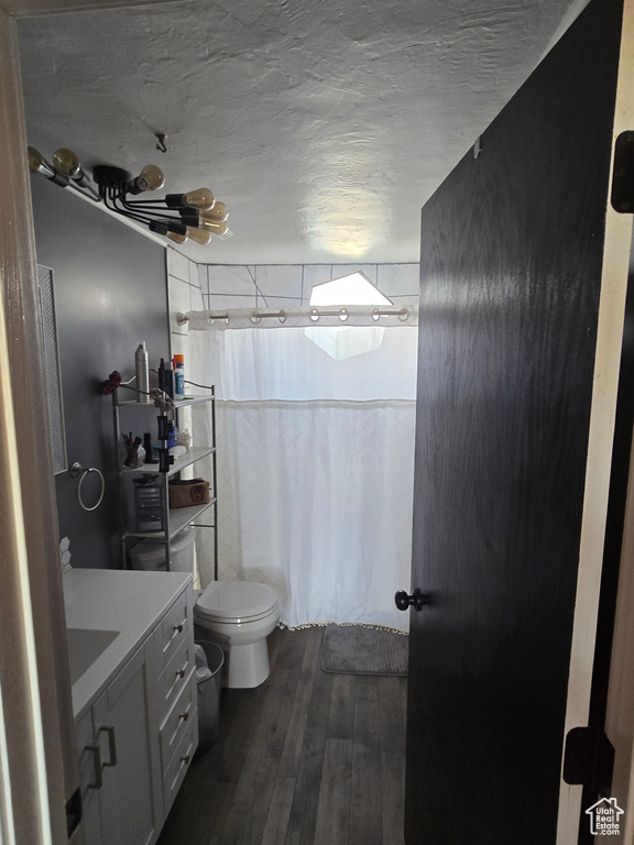 Full bathroom with wood-type flooring, toilet, vanity, and a textured ceiling