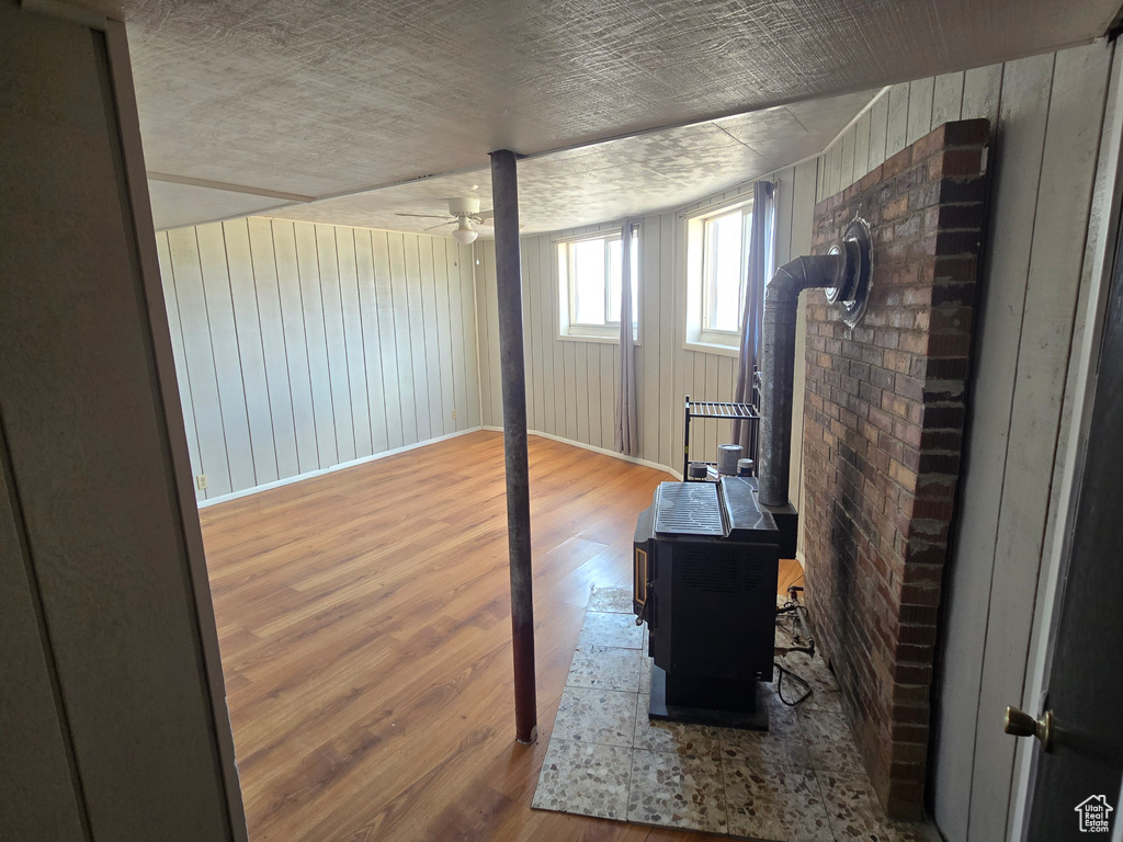 Interior space with wood finished floors, wood walls, ceiling fan, and a wood stove