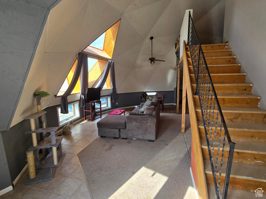 Living room with a ceiling fan, tile patterned flooring, lofted ceiling, and stairs