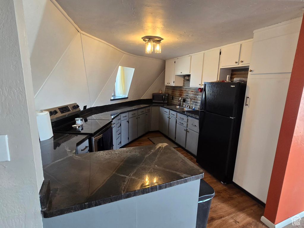 Kitchen featuring dark wood finished floors, decorative backsplash, a sink, dark countertops, and appliances with stainless steel finishes