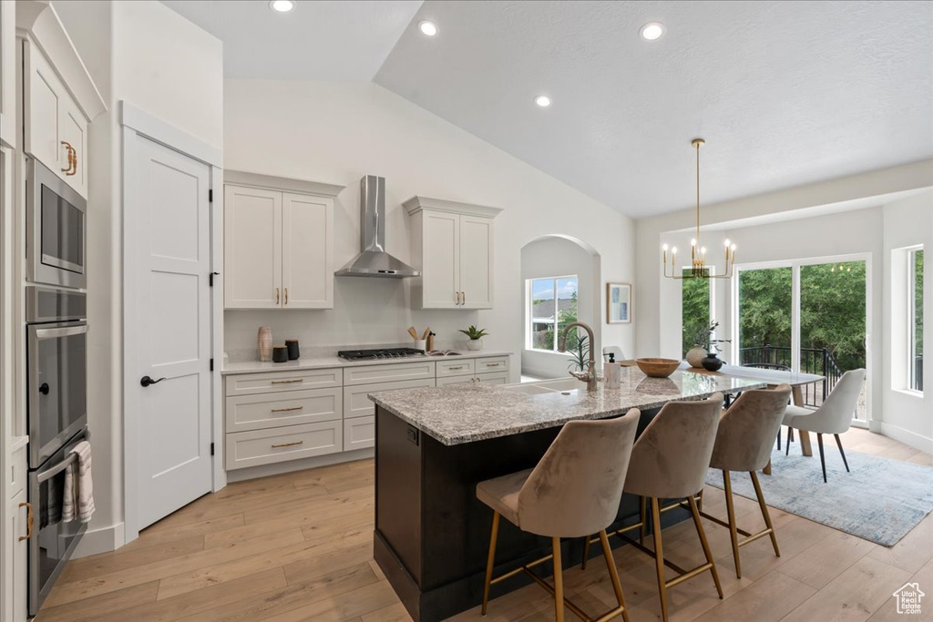 Kitchen with wall chimney range hood, a sink, stainless steel appliances, a chandelier, and light wood-style floors