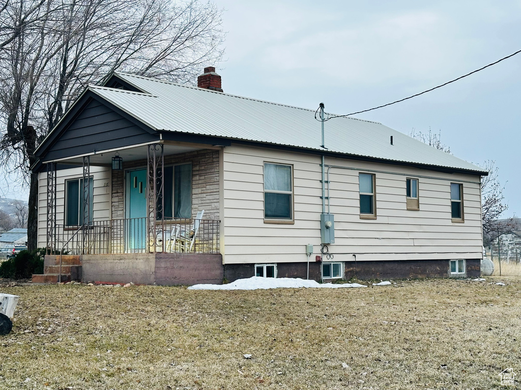 View of front of house with covered porch, a chimney, and metal roof