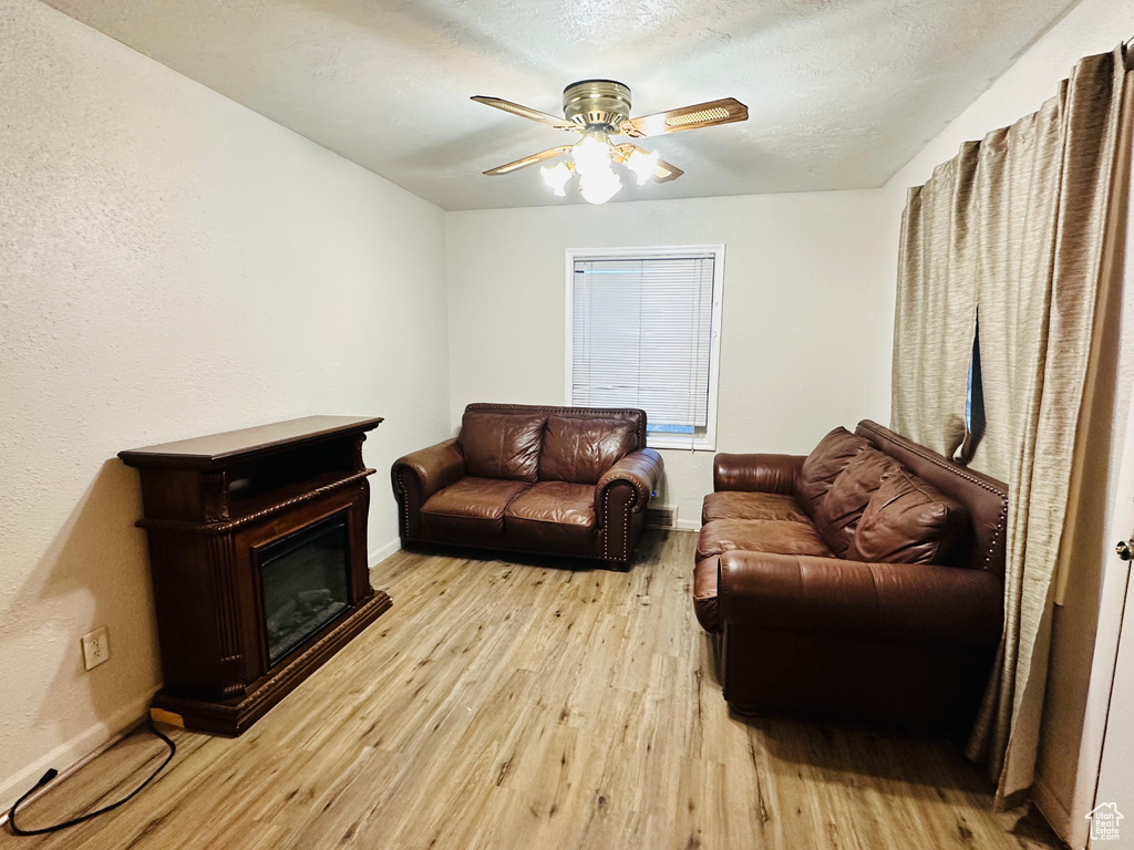Living room featuring a ceiling fan, a glass covered fireplace, baseboards, and light wood finished floors