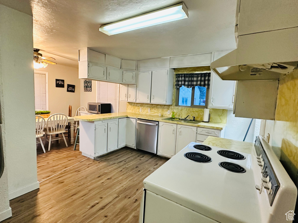 Kitchen featuring light countertops, white cabinetry, a peninsula, under cabinet range hood, and stainless steel appliances