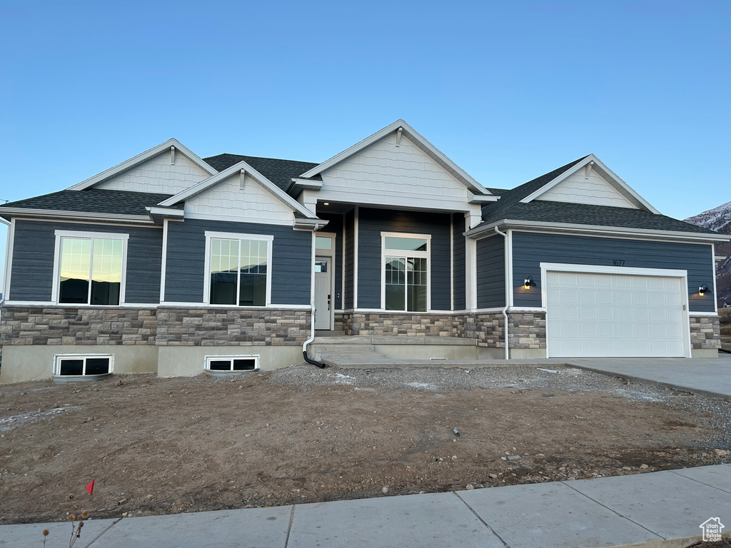 View of front of house featuring stone siding, a garage, concrete driveway, and roof with shingles