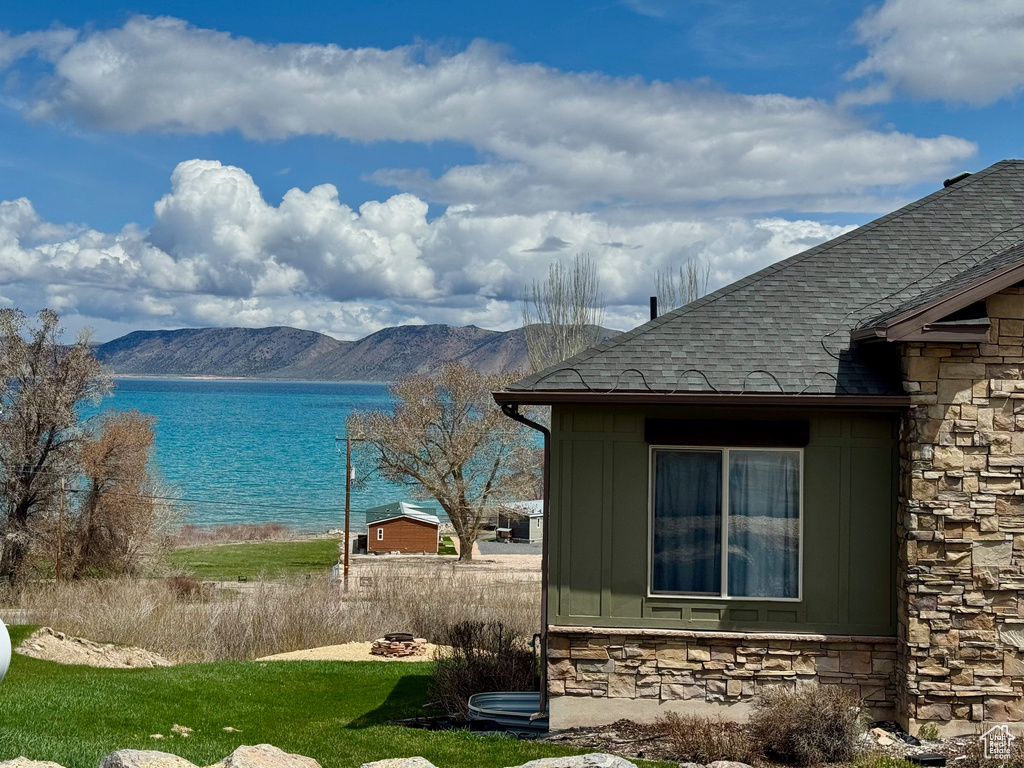 View of home's exterior featuring a water and mountain view, board and batten siding, roof with shingles, and stone siding