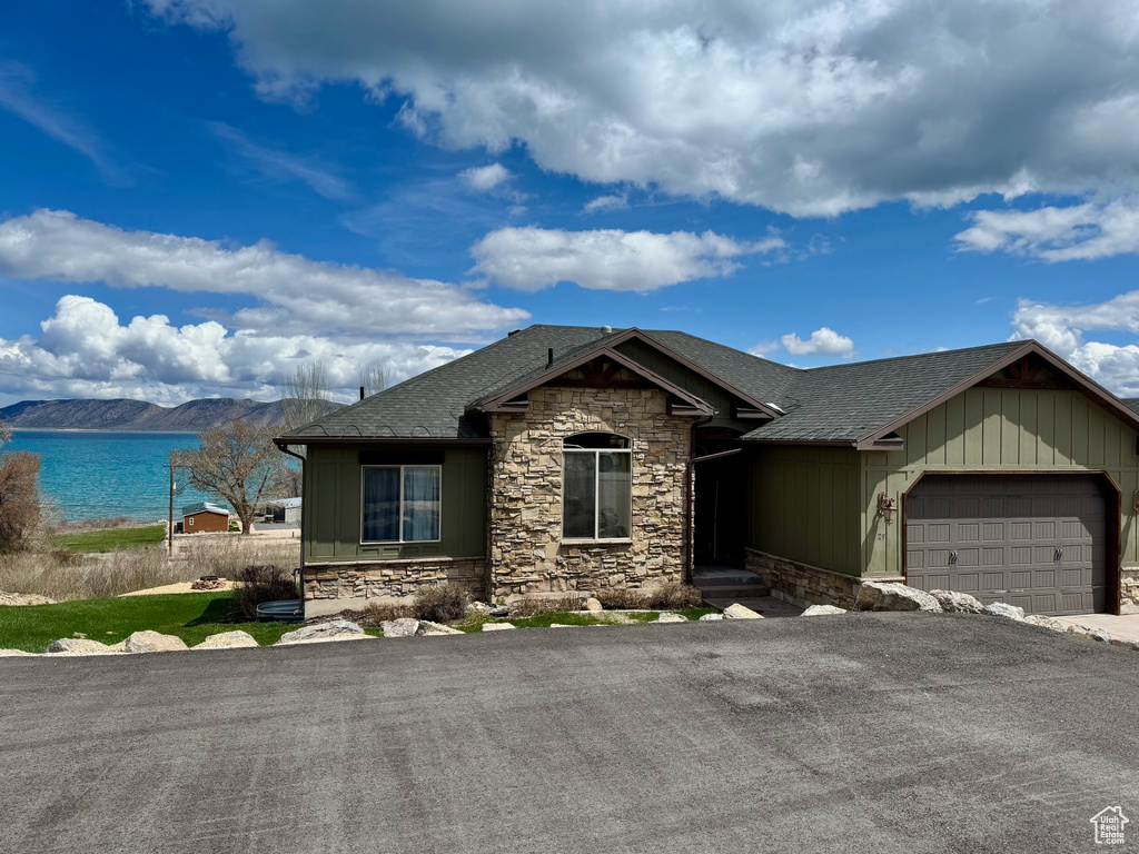 Ranch-style home with a garage, stone siding, a shingled roof, a water view, and driveway