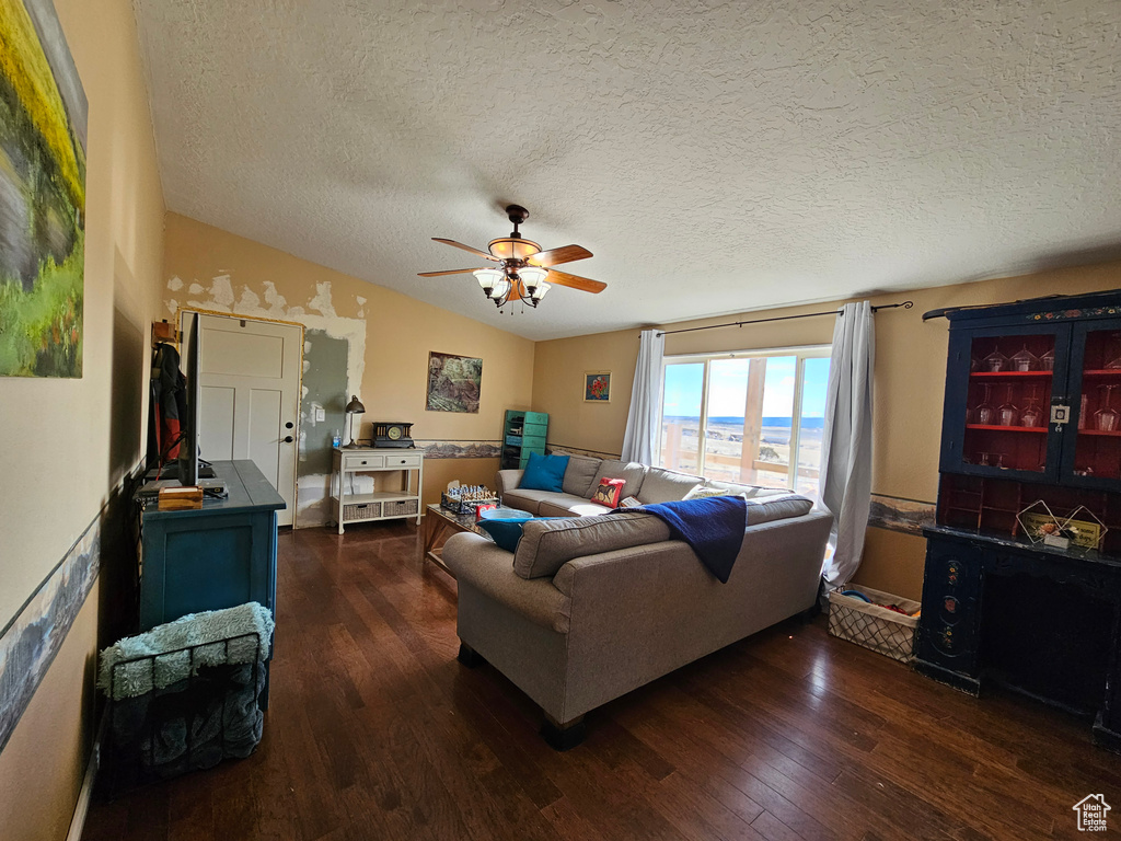 Living room with a textured ceiling, vaulted ceiling, a ceiling fan, and dark wood finished floors