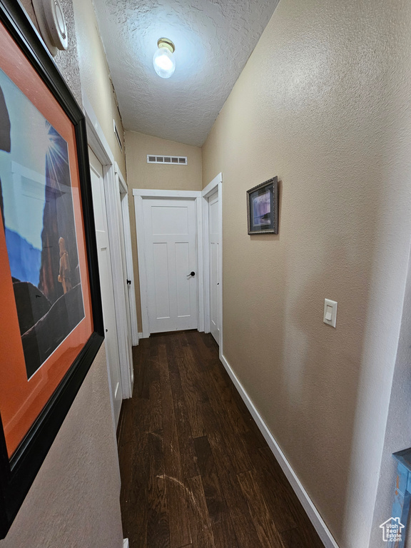 Hall featuring lofted ceiling, baseboards, a textured ceiling, visible vents, and wood finished floors