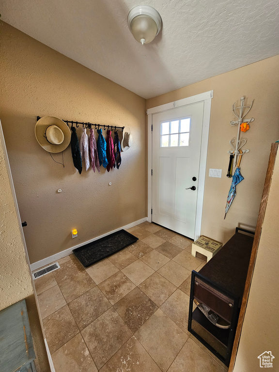 Doorway featuring a textured wall, a textured ceiling, baseboards, and visible vents