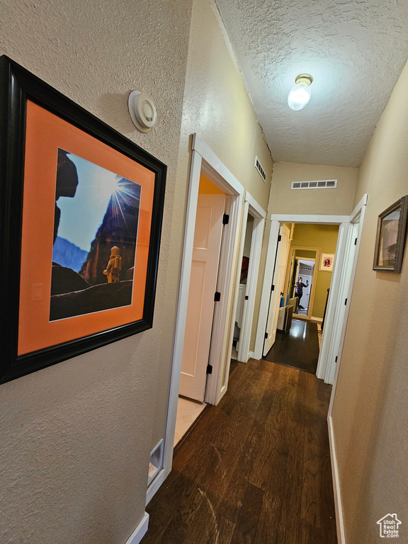 Hall featuring baseboards, visible vents, wood finished floors, and a textured ceiling