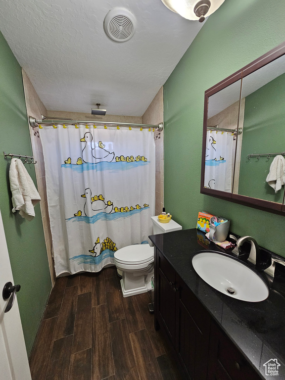 Full bath with a shower with shower curtain, vanity, a textured ceiling, wood finish floors, and visible vents