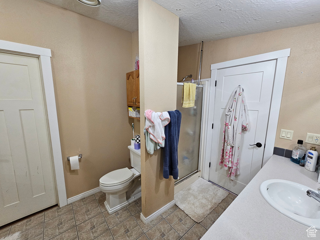 Bathroom featuring vanity, toilet, baseboards, a textured ceiling, and a shower stall