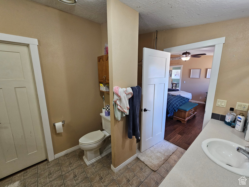 Bathroom with a textured ceiling, baseboards, ceiling fan, toilet, and vanity