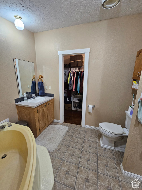 Full bath with a textured ceiling, baseboards, toilet, vanity, and a spacious closet