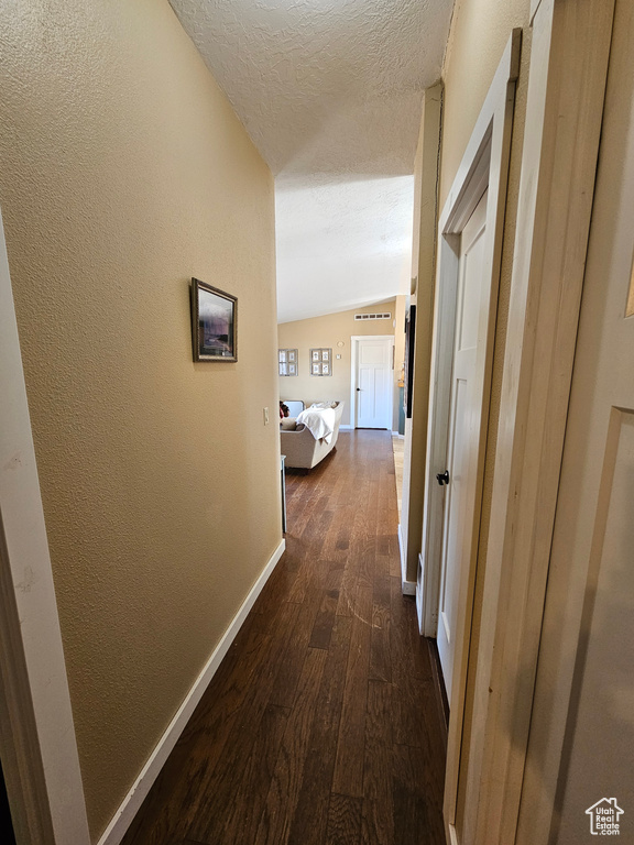 Hallway with a textured ceiling, baseboards, dark wood-style floors, a textured wall, and vaulted ceiling
