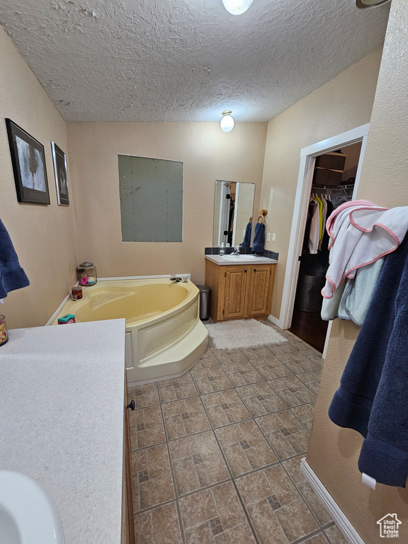 Full bathroom featuring vanity, a spacious closet, baseboards, a textured ceiling, and a bath