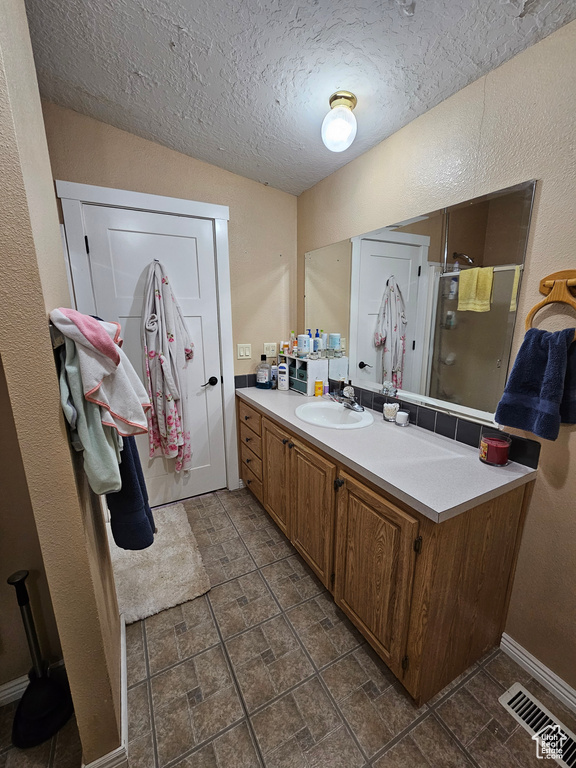 Full bathroom featuring a textured ceiling, visible vents, a shower stall, baseboards, and vanity
