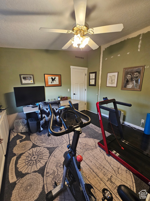 Exercise room with baseboards, visible vents, ceiling fan, and a textured ceiling