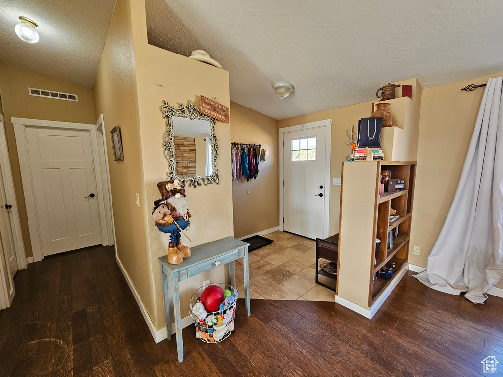 Foyer featuring vaulted ceiling, baseboards, a textured ceiling, visible vents, and wood finished floors