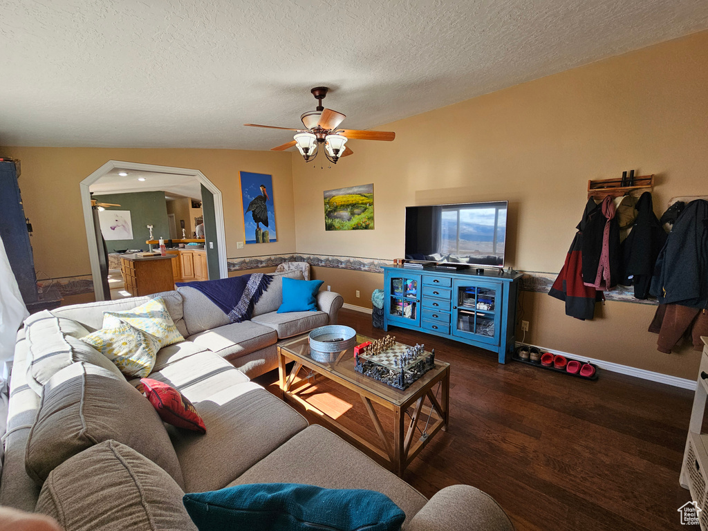 Living room with wood finished floors, a textured ceiling, baseboards, arched walkways, and ceiling fan