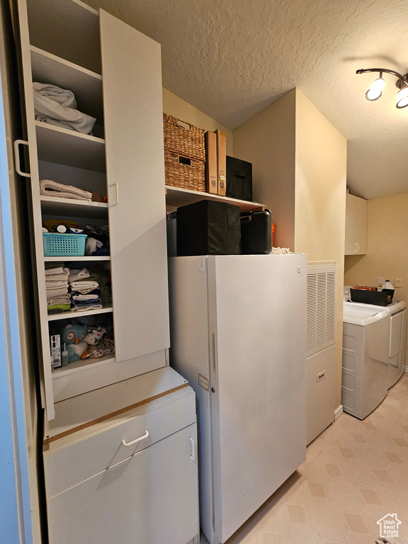 Clothes washing area featuring light floors, cabinet space, washer and dryer, and a textured ceiling