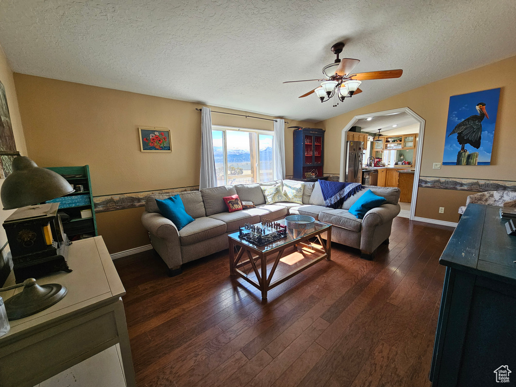 Living area with dark wood-style flooring, arched walkways, a textured ceiling, and ceiling fan