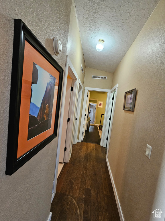 Corridor featuring a textured wall, baseboards, a textured ceiling, visible vents, and wood finished floors