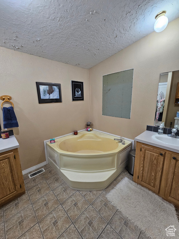 Bathroom with vanity, a garden tub, a textured ceiling, baseboards, and visible vents