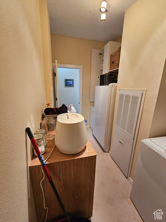 Laundry area featuring a textured wall, a textured ceiling, washer / dryer, laundry area, and light floors