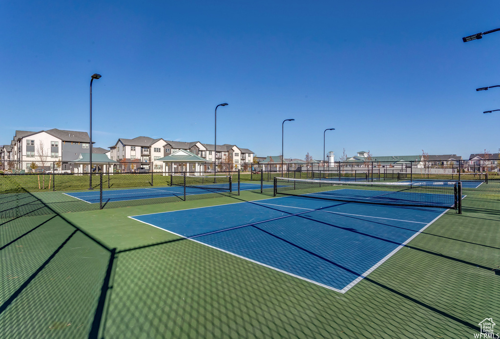 View of tennis court with a residential view and fence