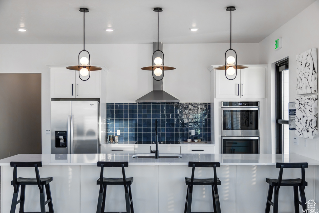 Kitchen with a sink, pendant lighting, white cabinetry, appliances with stainless steel finishes, and decorative backsplash