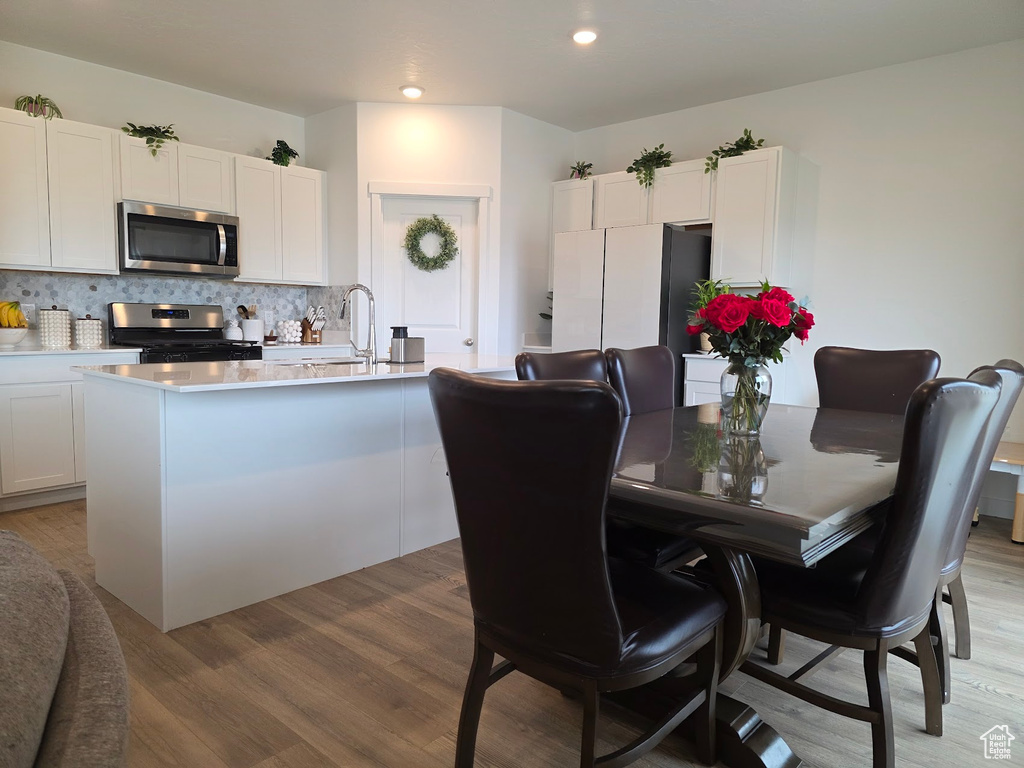 Kitchen featuring light countertops, tasteful backsplash, light wood finished floors, white cabinets, and appliances with stainless steel finishes