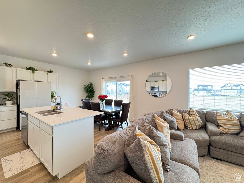 Kitchen with white cabinets, light wood-style flooring, dishwasher, a sink, and open floor plan