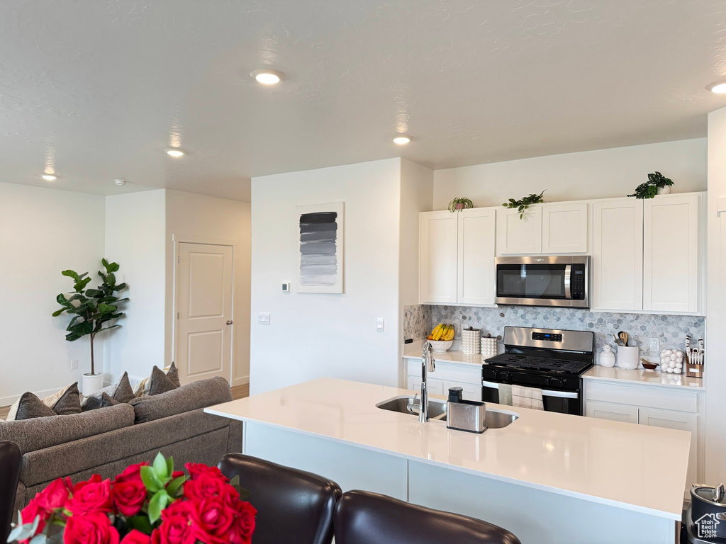Kitchen with a sink, white cabinetry, tasteful backsplash, a kitchen breakfast bar, and appliances with stainless steel finishes