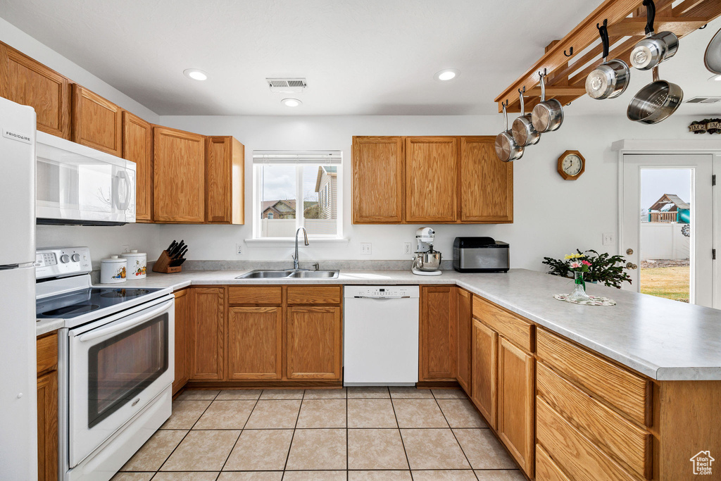 Kitchen with light tile patterned flooring, a sink, a peninsula, white appliances, and visible vents
