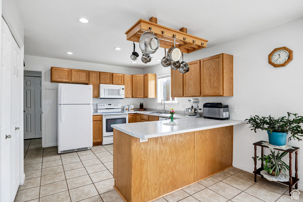 Kitchen with light tile patterned floors, light countertops, a peninsula, and white appliances