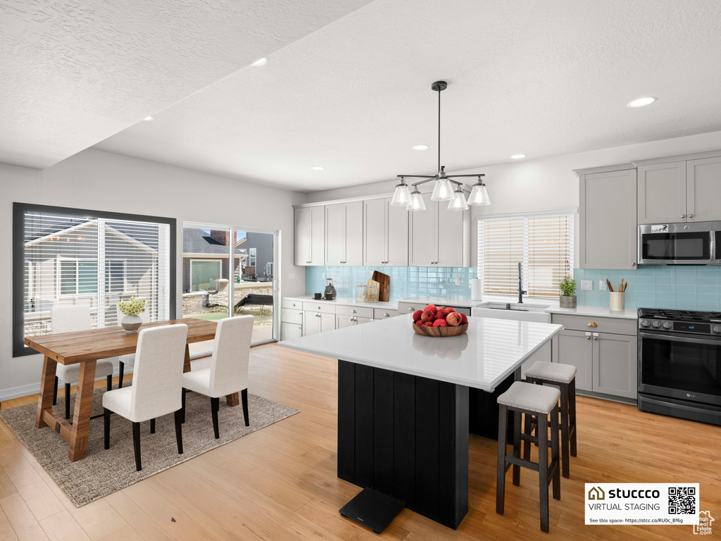 Kitchen featuring appliances with stainless steel finishes, a sink, gray cabinets, light countertops, and decorative backsplash