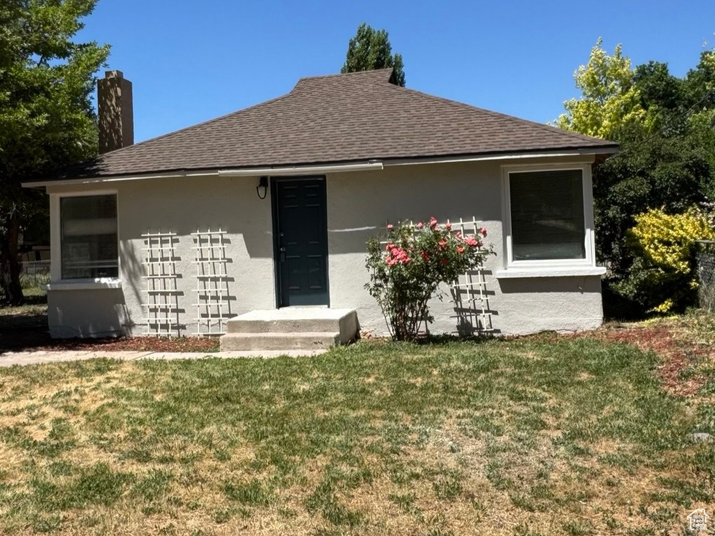 View of front of property with a front lawn, stucco siding, a chimney, and roof with shingles