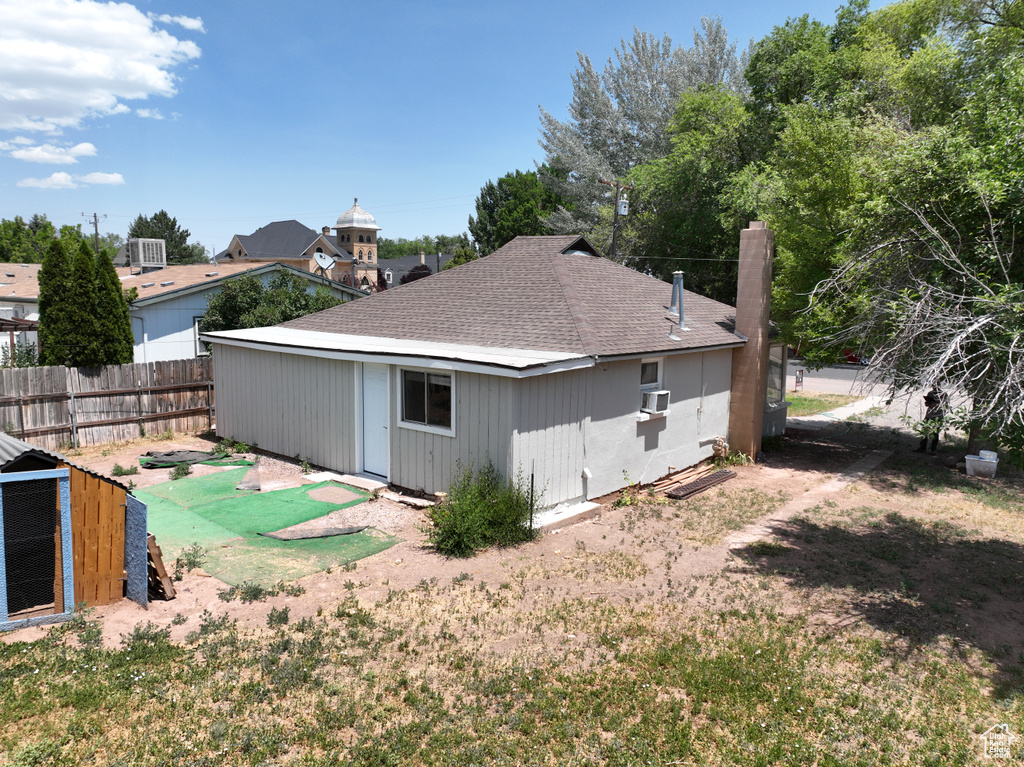 Back of property featuring a shingled roof, a chimney, an outdoor structure, and cooling unit