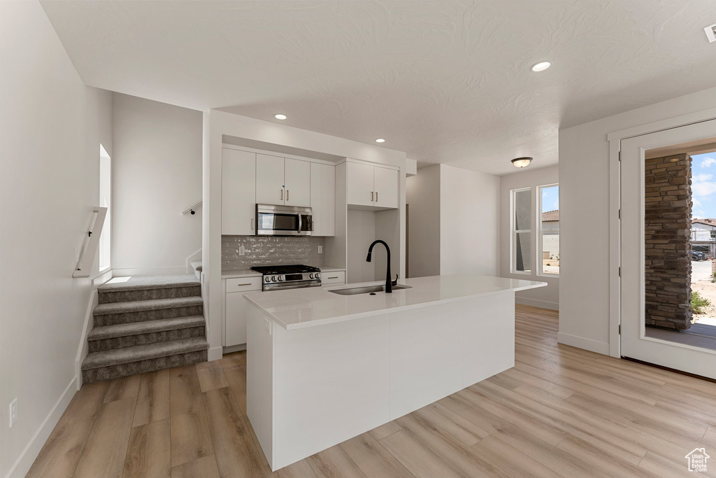 Kitchen featuring appliances with stainless steel finishes, white cabinets, light wood-type flooring, tasteful backsplash, and light countertops