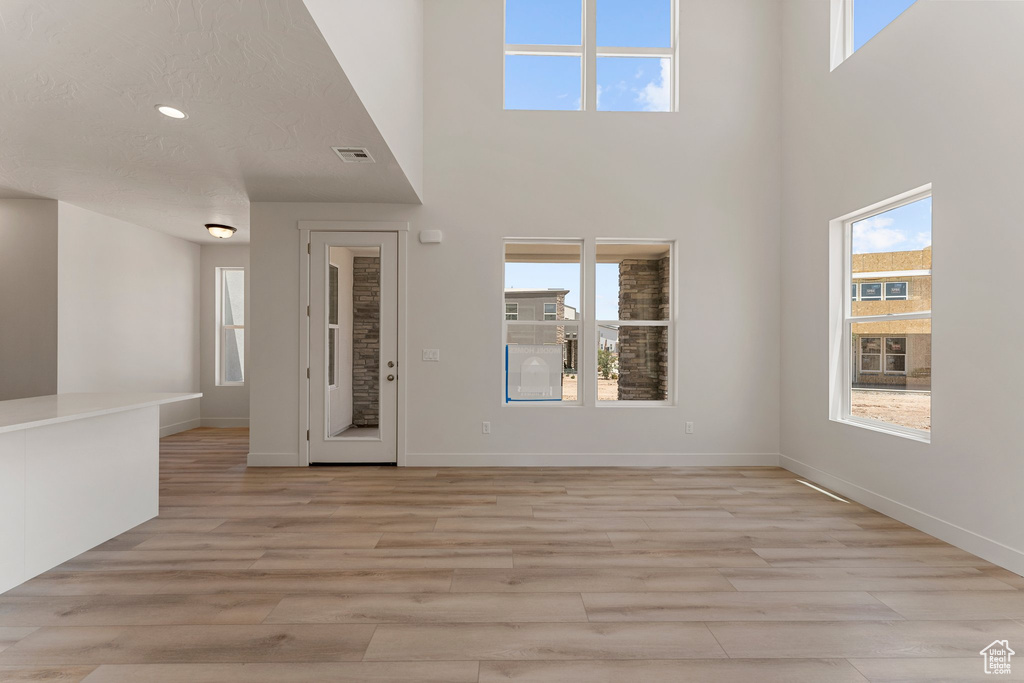 Unfurnished living room featuring a high ceiling, light wood finished floors, and recessed lighting