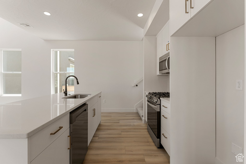 Kitchen featuring stainless steel appliances, light wood finished floors, recessed lighting, white cabinetry, and a center island with sink