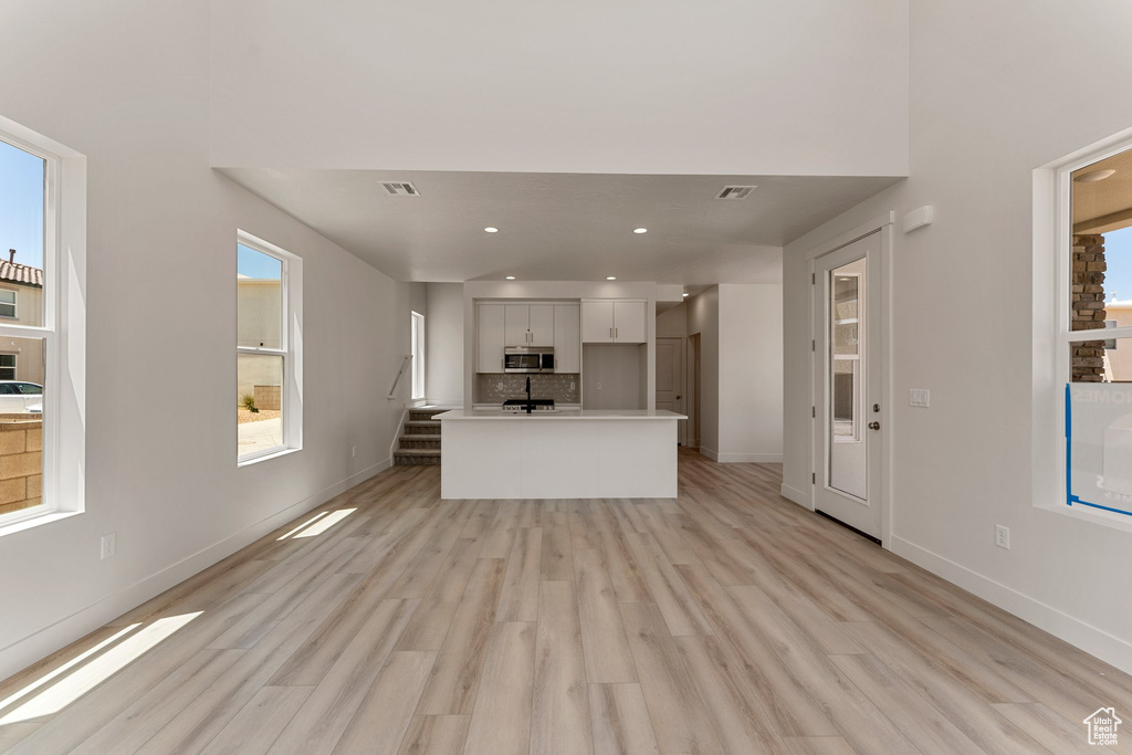 Kitchen featuring stainless steel microwave, light wood-style floors, decorative backsplash, light countertops, and recessed lighting