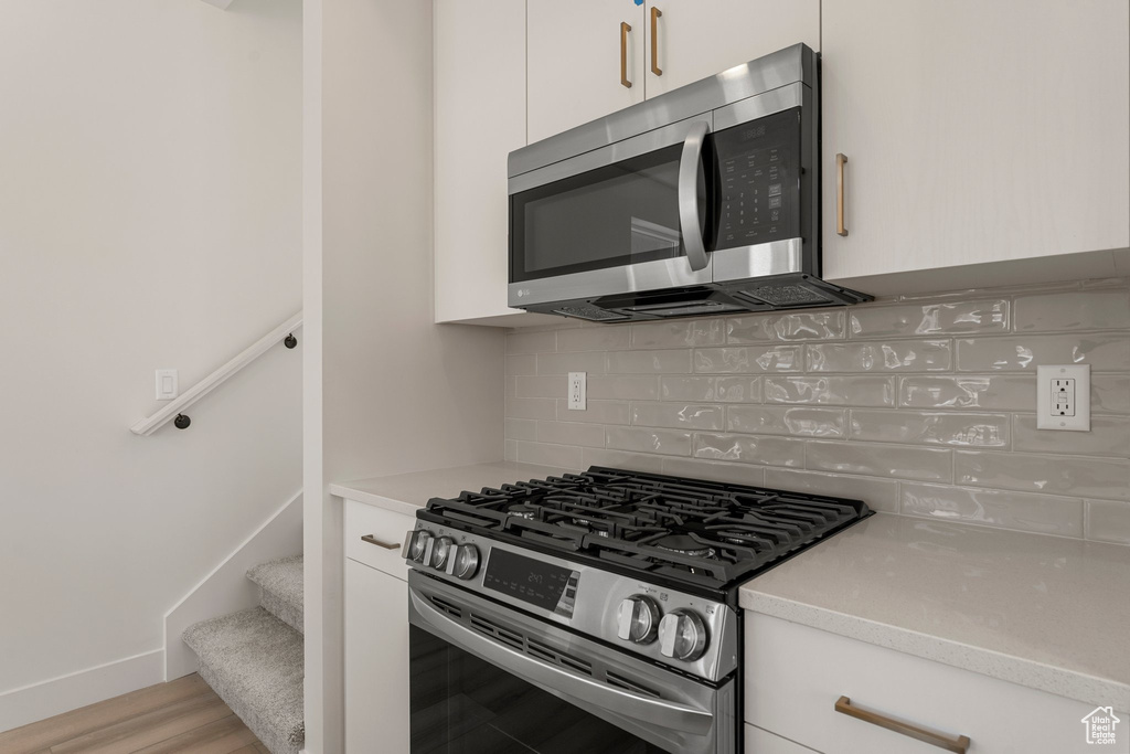 Kitchen featuring appliances with stainless steel finishes, tasteful backsplash, light countertops, and white cabinetry