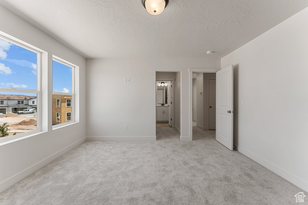 Unfurnished bedroom featuring light carpet, a textured ceiling, and ensuite bathroom