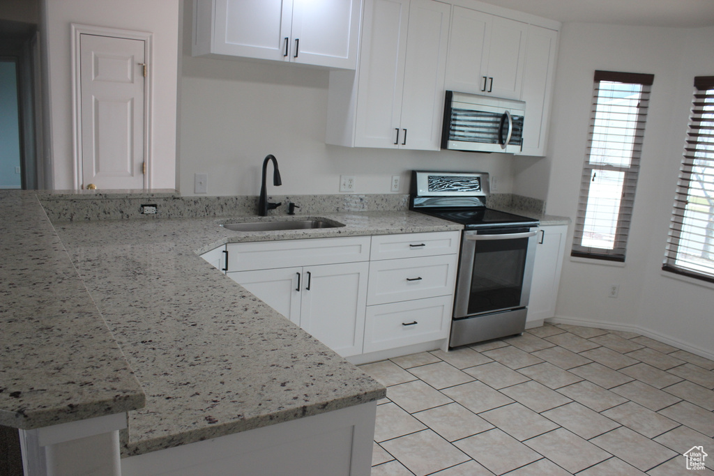 Kitchen featuring light stone counters, a sink, white cabinetry, a peninsula, and stainless steel appliances