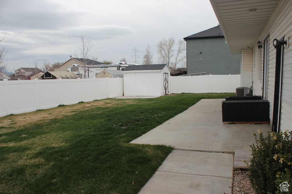 View of yard featuring a storage shed, central AC, a fenced backyard, an outbuilding, and a patio area
