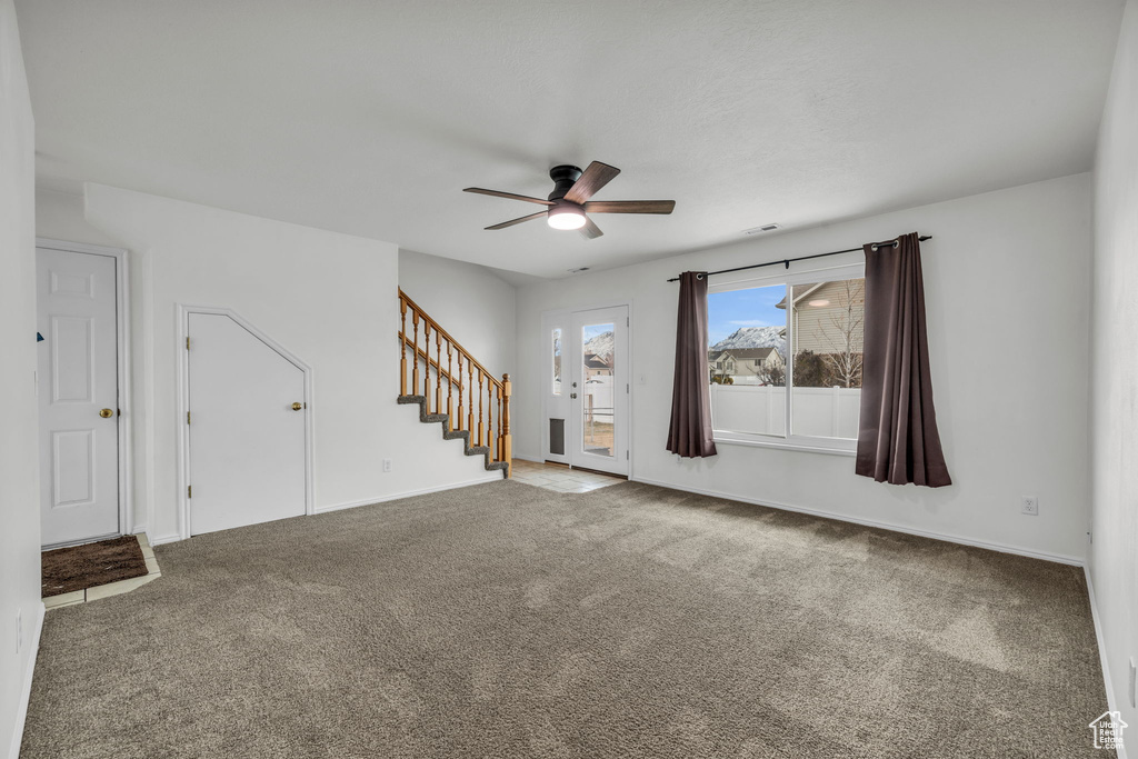 Unfurnished living room featuring baseboards, stairs, ceiling fan, and carpet flooring